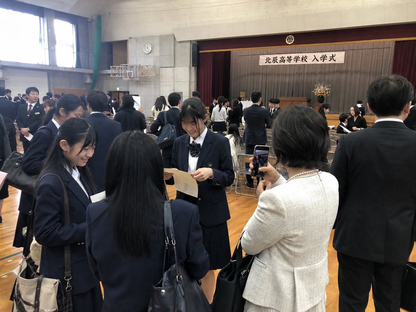 式典開始前、体育館で資料を確認する新入生と保護者
